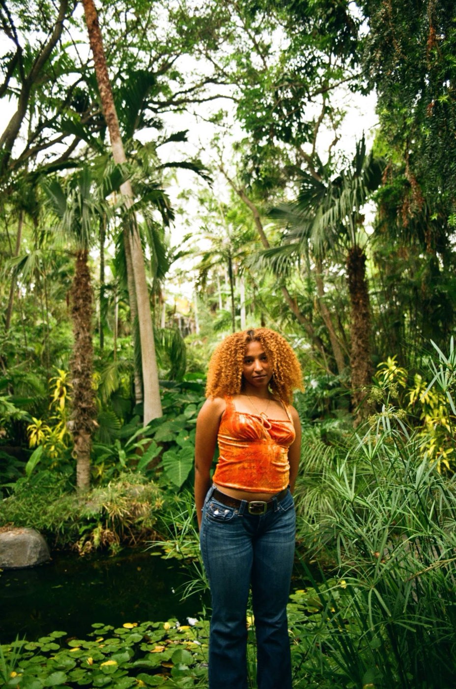 Nicole Hernandez in an orange top among palms and a lily pond