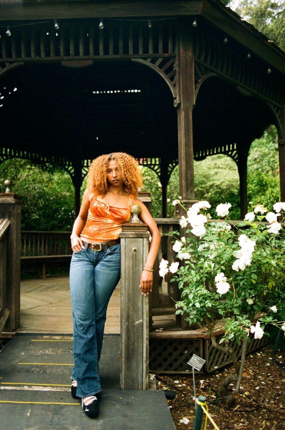 Nicole Hernandez leaning on a wooden gazebo beside white roses